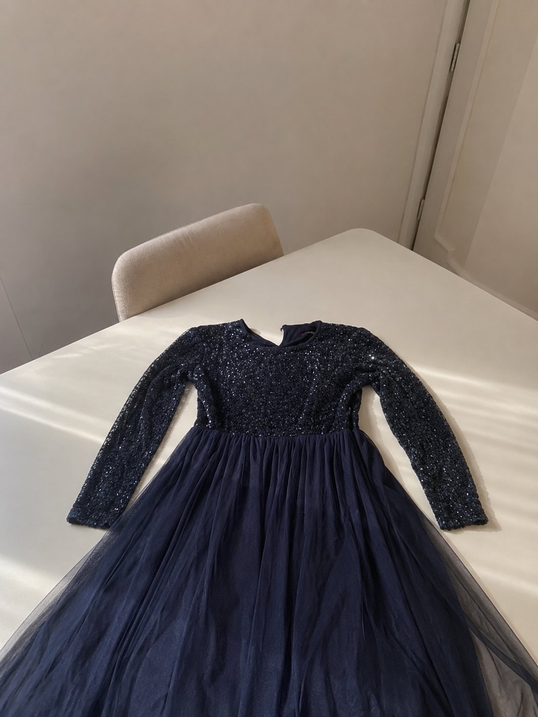 C’est une longue robe de soirée de couleur bleu marine (bleu foncé), avec un haut brillant orné de sequins et des manches longues, ainsi qu’une jupe volumineuse en tulle doux.