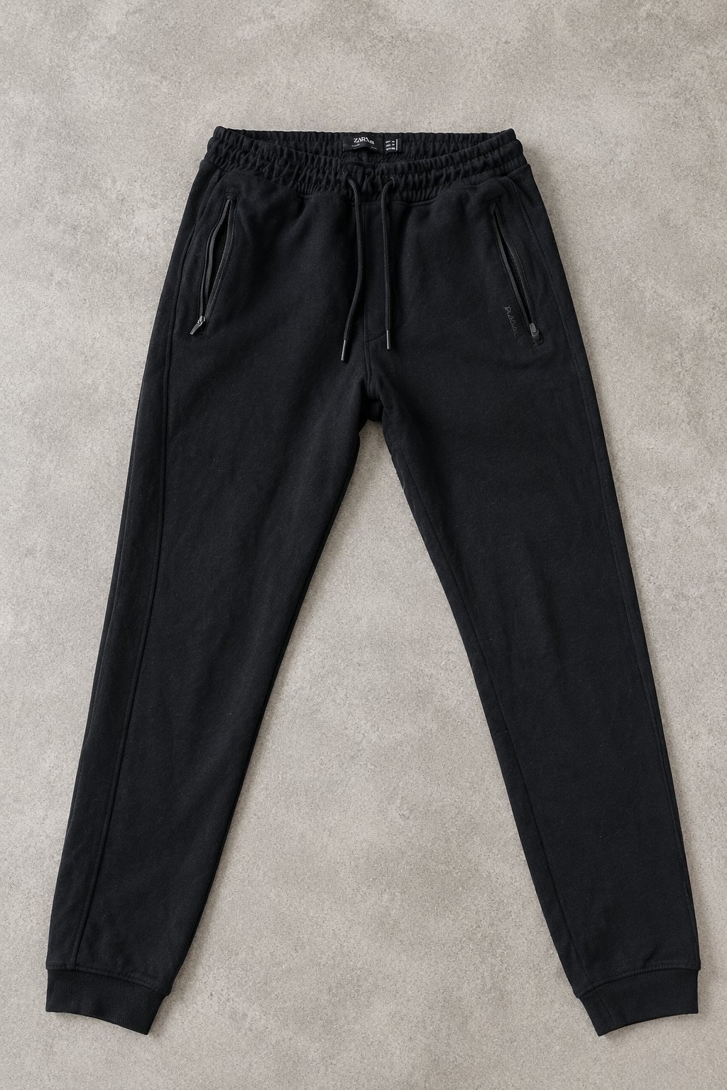 Jogging Pull&Bear noir, confortable et stylé, avec poches zippées et taille élastique à cordon. Idéal pour un look sportif et décontracté.