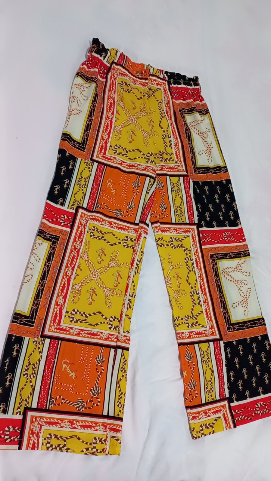 Pantalon fluide à jambes larges de la marque 101 Idées se distingue par son imprimé baroque en patchwork coloré mêlant des motifs de chaînes et de cordages rétro.