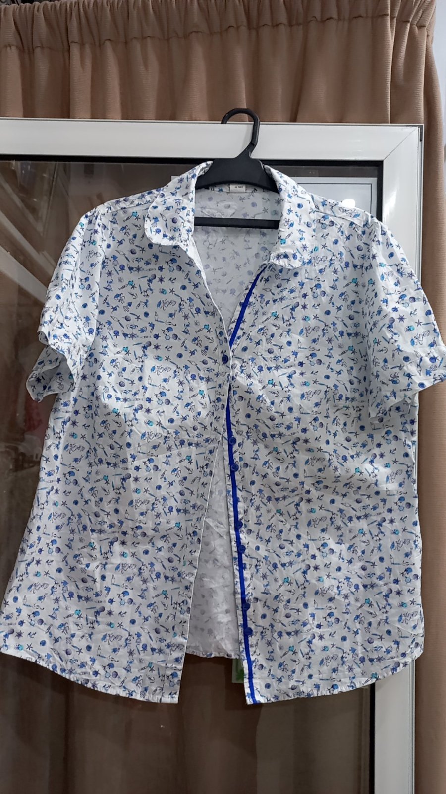 Chemise blanche décontractée présente un motif marin bleu complexe, avec des détails charmants comme des ancres et des poissons.   