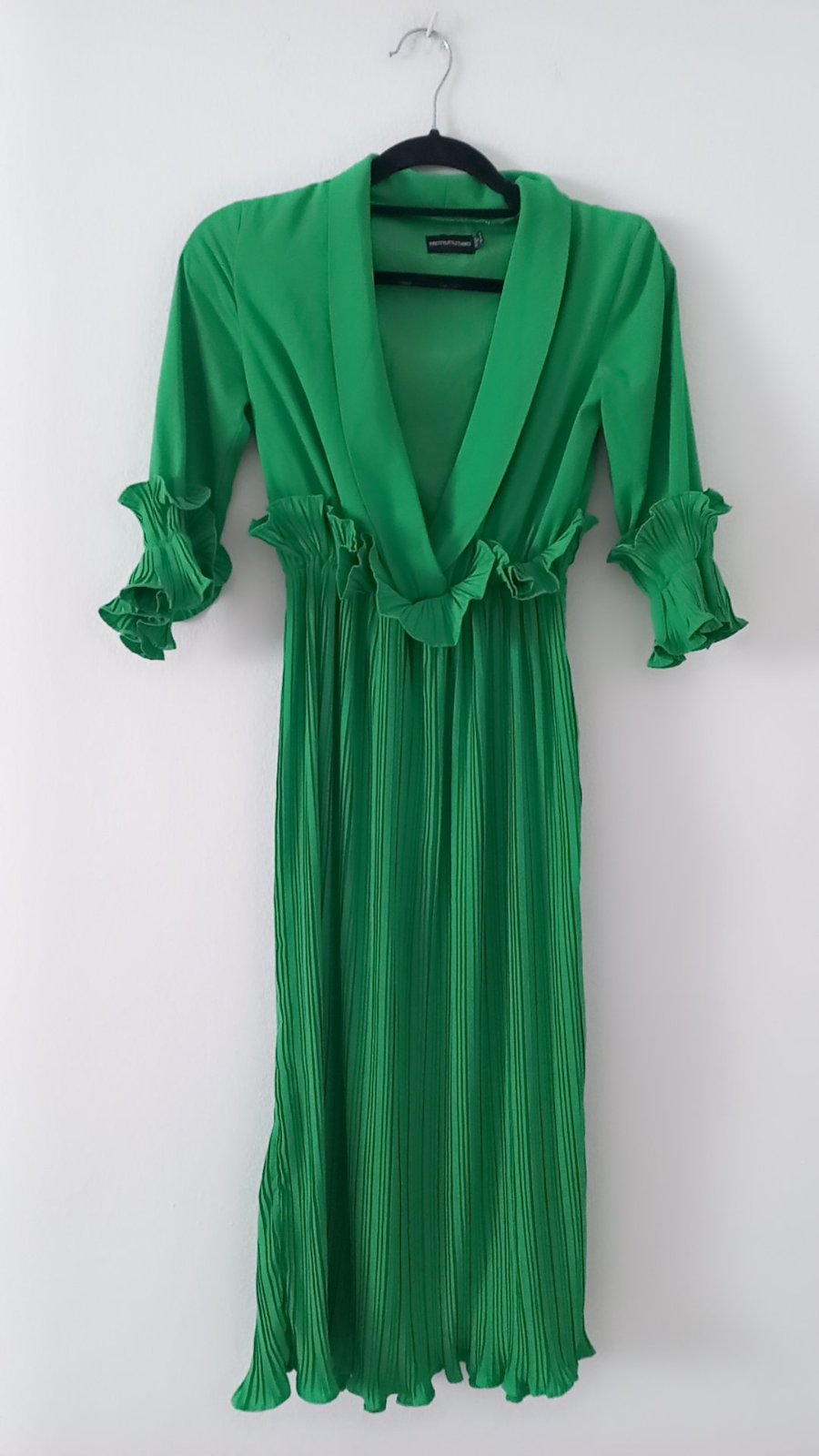  une robe mi-longue plissée vert émeraude de style cache-cœur avec des volants à la taille et aux poignets.