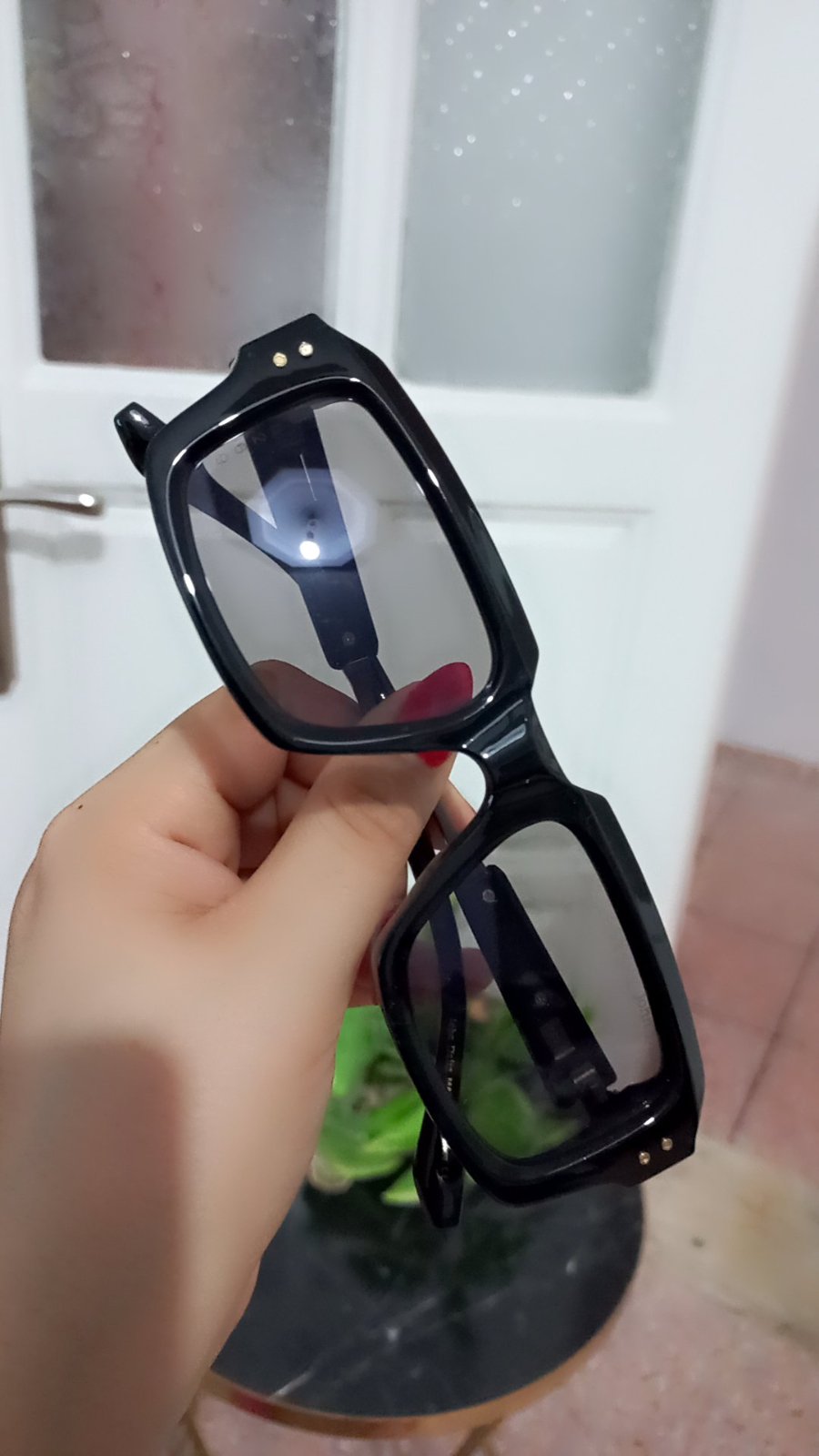 Lunettes de soleil carrées de style rétro se distinguent par leur monture noire épaisse en acétate et leurs verres teintés dotés de petits rivets métalliques décoratifs sur les coins supérieurs.