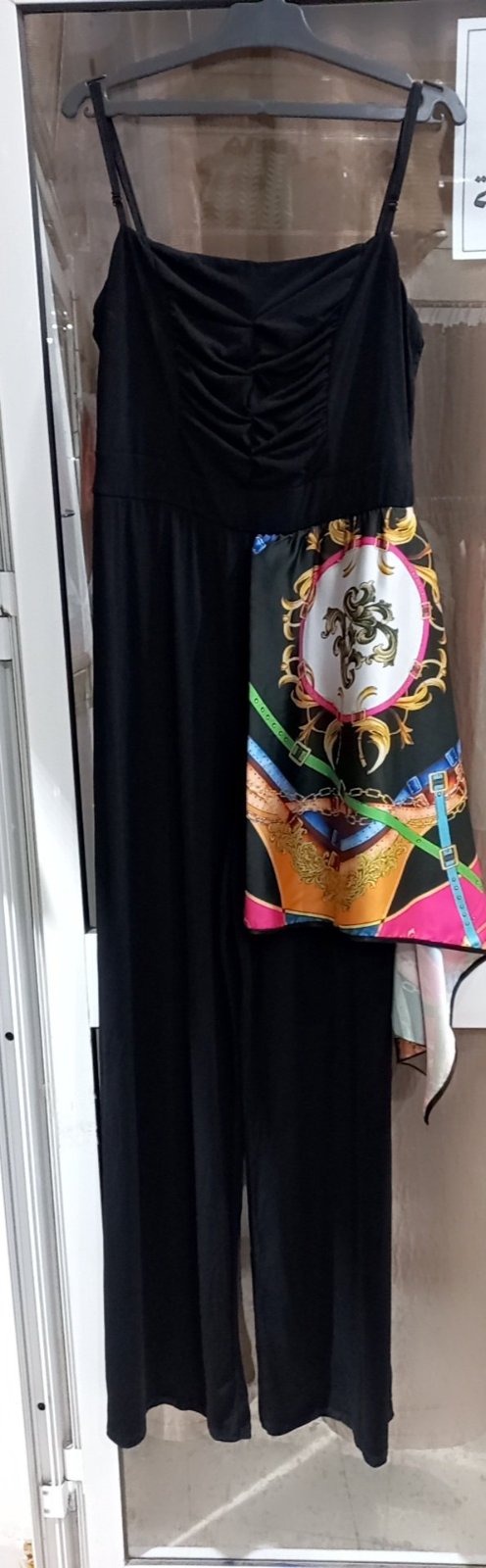 Combinaison pantalon de couleur noire, ornée d'un imprimé foulard coloré sur le côté droit. La combinaison est sans manches avec des bretelles fines, et le tissu de la partie supérieure semble légèrement froncé. 