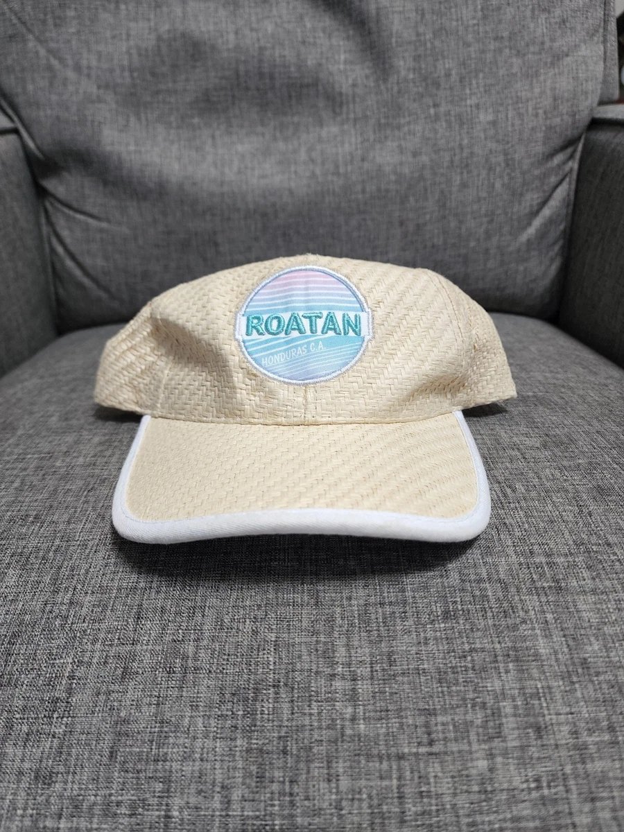 Casquette est une casquette de style "trucker" en paille de couleur beige avec un logo bleu clair portant la mention "Roatan Honduras CA".