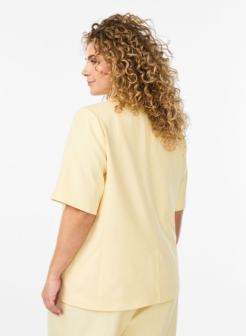 Chemise jaune clair à manches courtes présente une encolure en V et une fermeture à bouton unique,