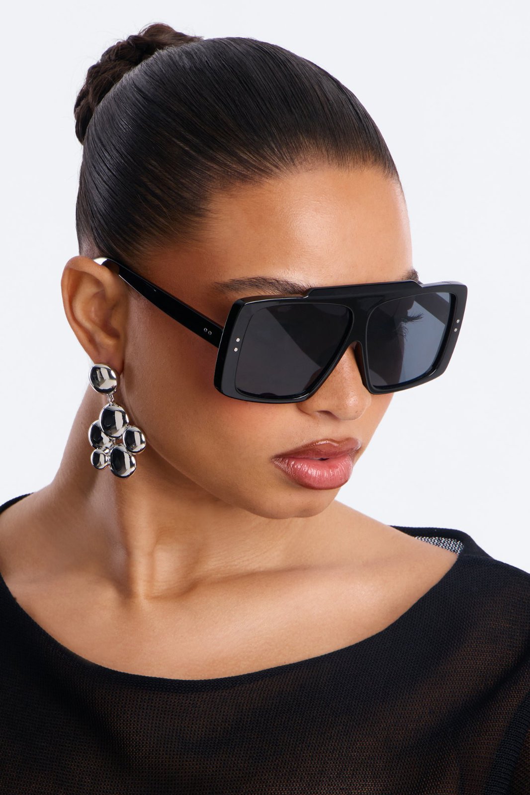 Lunettes de soleil oversize de style aviateur/carré se caractérisent par leur monture épaisse en acétate noir rigide, un pont supérieur plat surélevé et deux petits rivets métalliques argentés visibles de chaque côté de la face avant.