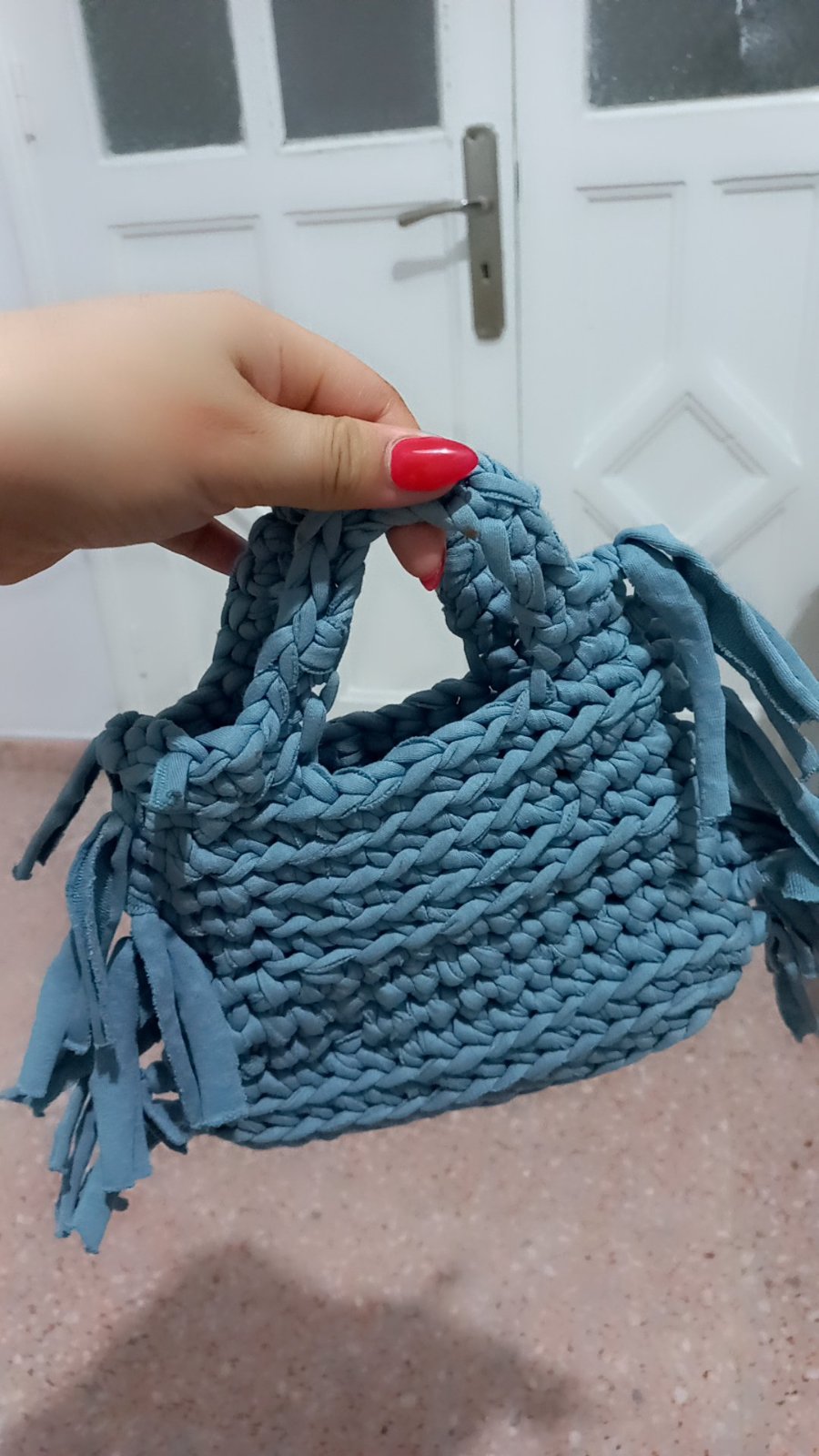 Sac à main artisanal fait main est tricoté ou crocheté en mailles épaisses à l'aide d'un fil de trapilho (fil de T-shirt) bleu ciel texturé et se distingue par ses finitions originales à franges latérales décoratives.