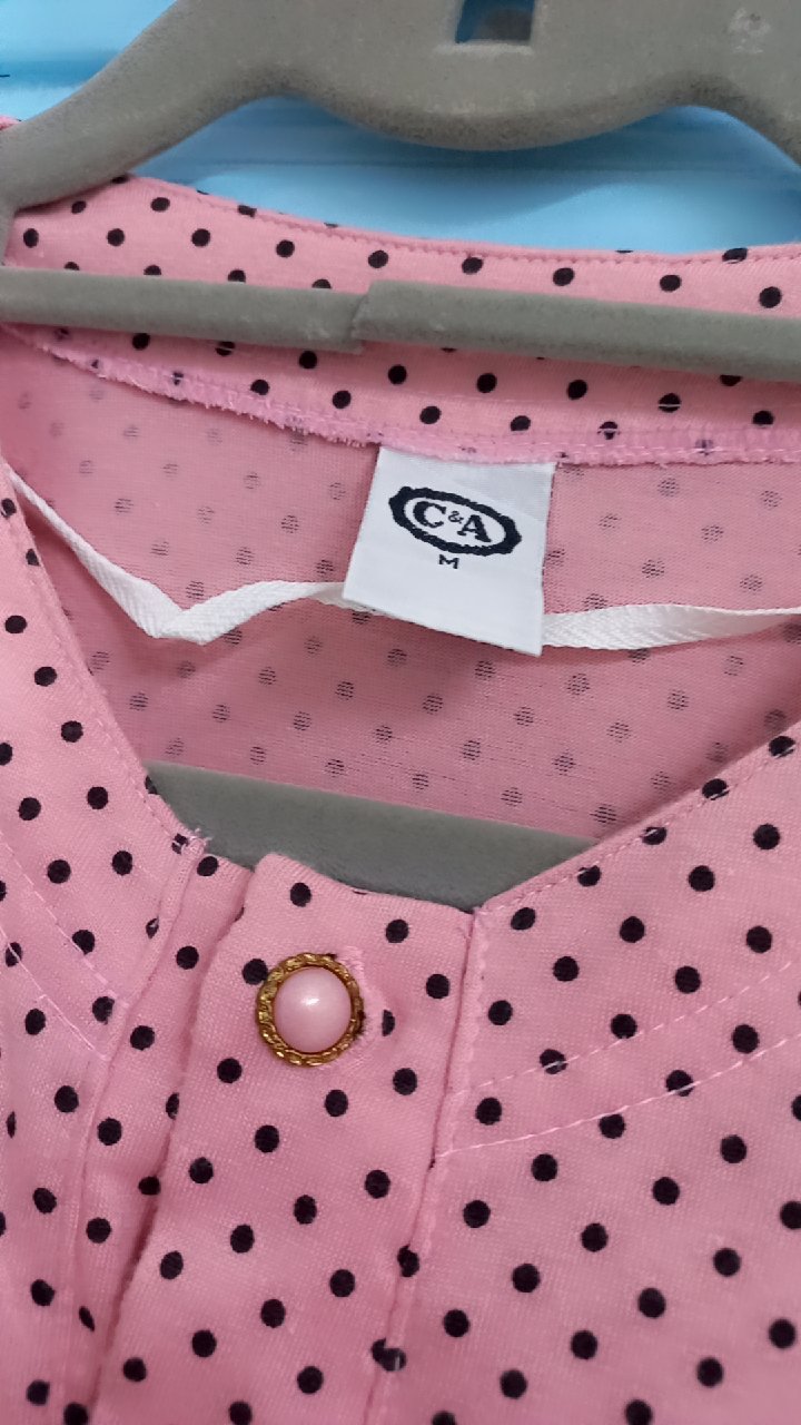 Un chemisier rose avec des pois noirs, probablement de la marque C&A, arborant deux poches poitrine et un col boutonné