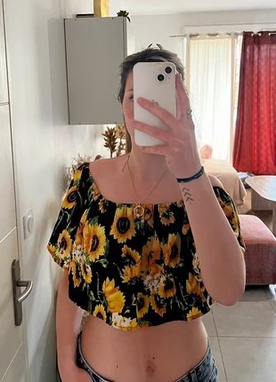 Magnifique blouse noire à épaules dénudées présente un imprimé vibrant de tournesols jaunes et est dotée d'un élégant volant. 