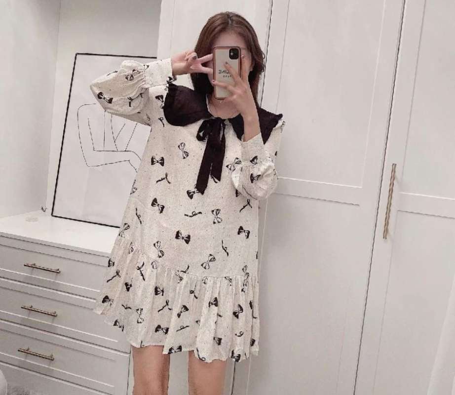 Robe est une mini-robe blanche de style coréen, caractérisée par un imprimé de petits nœuds noirs et un grand col contrasté avec un nœud papillon noir.