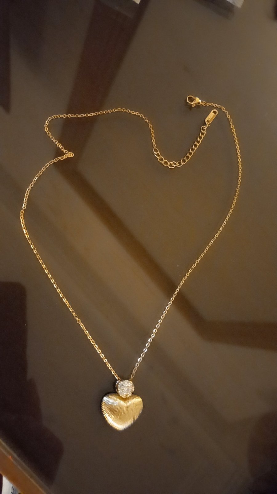 Collier doré en acier inoxydable présente un pendentif en forme de cœur texturé surmonté d'un petit élément brillant