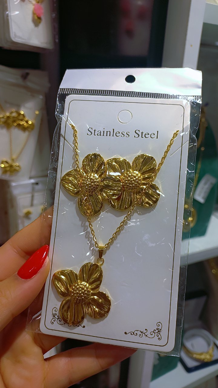 Parure en acier inoxydable doré de SHEIN comprend un collier et des boucles d'oreilles assorties arborant un motif de fleur stylisée avec un centre texturé.