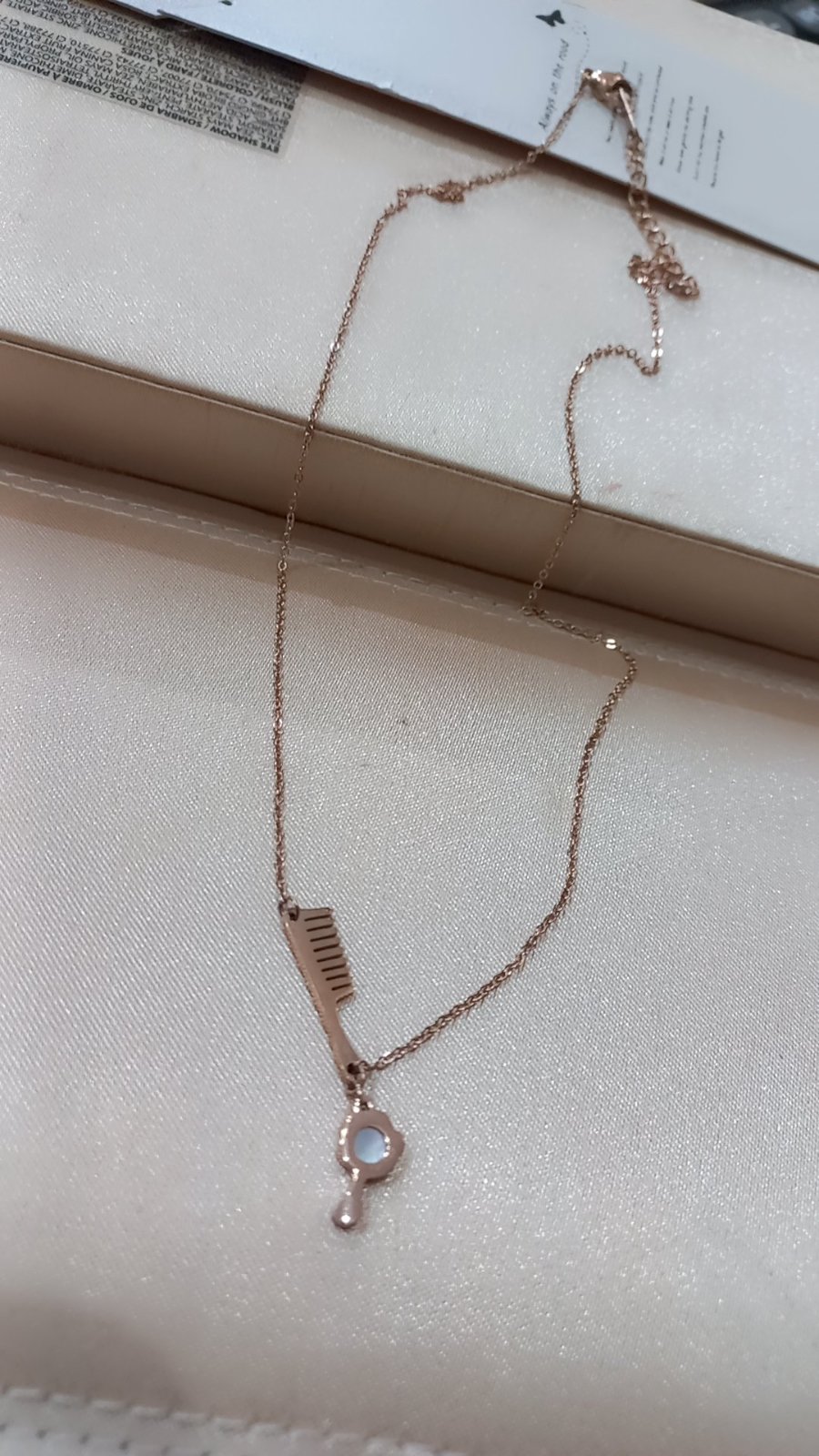 Collier inoxydable rose avec des pendentifs en forme de peigne et de miroir à main.