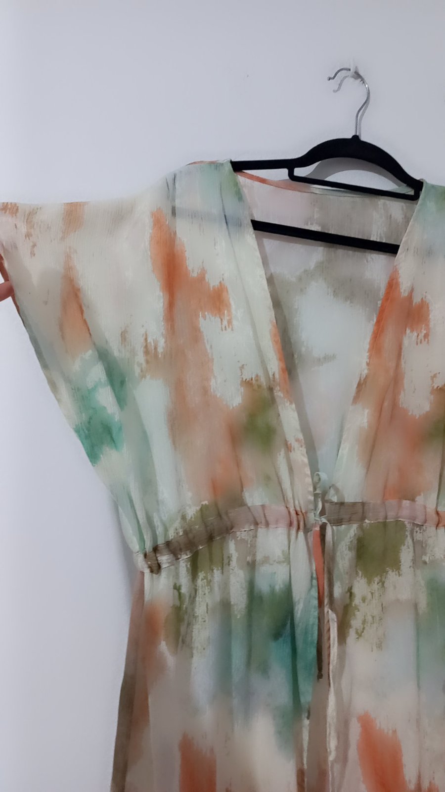 Un kimono long fluide pour femme, idéal comme tenue de plage par des manches courtes amples, une taille froncée élastique munie d'un cordon de serrage, et un imprimé tie-dye artistique aux nuances pastel d'orange, de vert sauge et de blanc.
