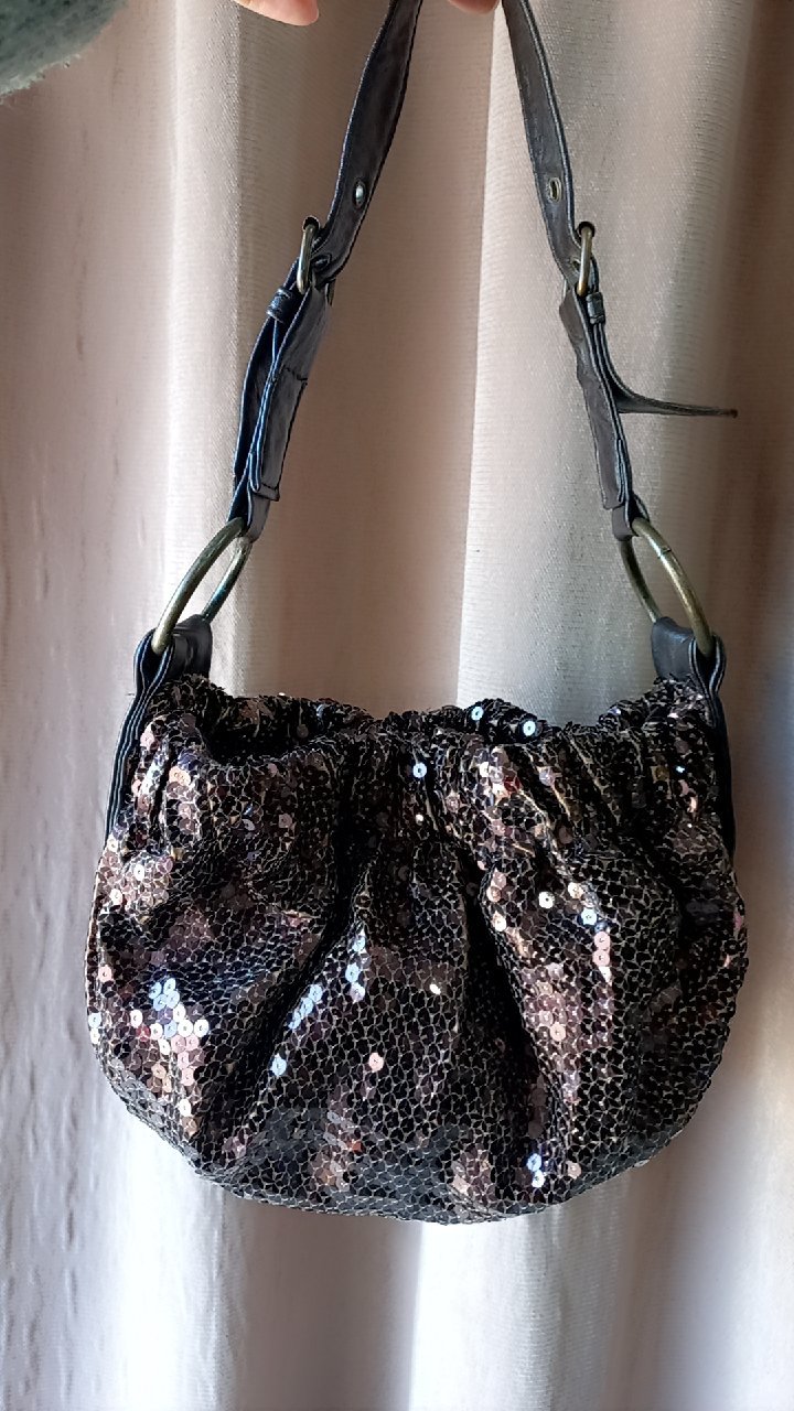 Sac à main à paillettes orné de cuir noir et de boucles métalliques. 