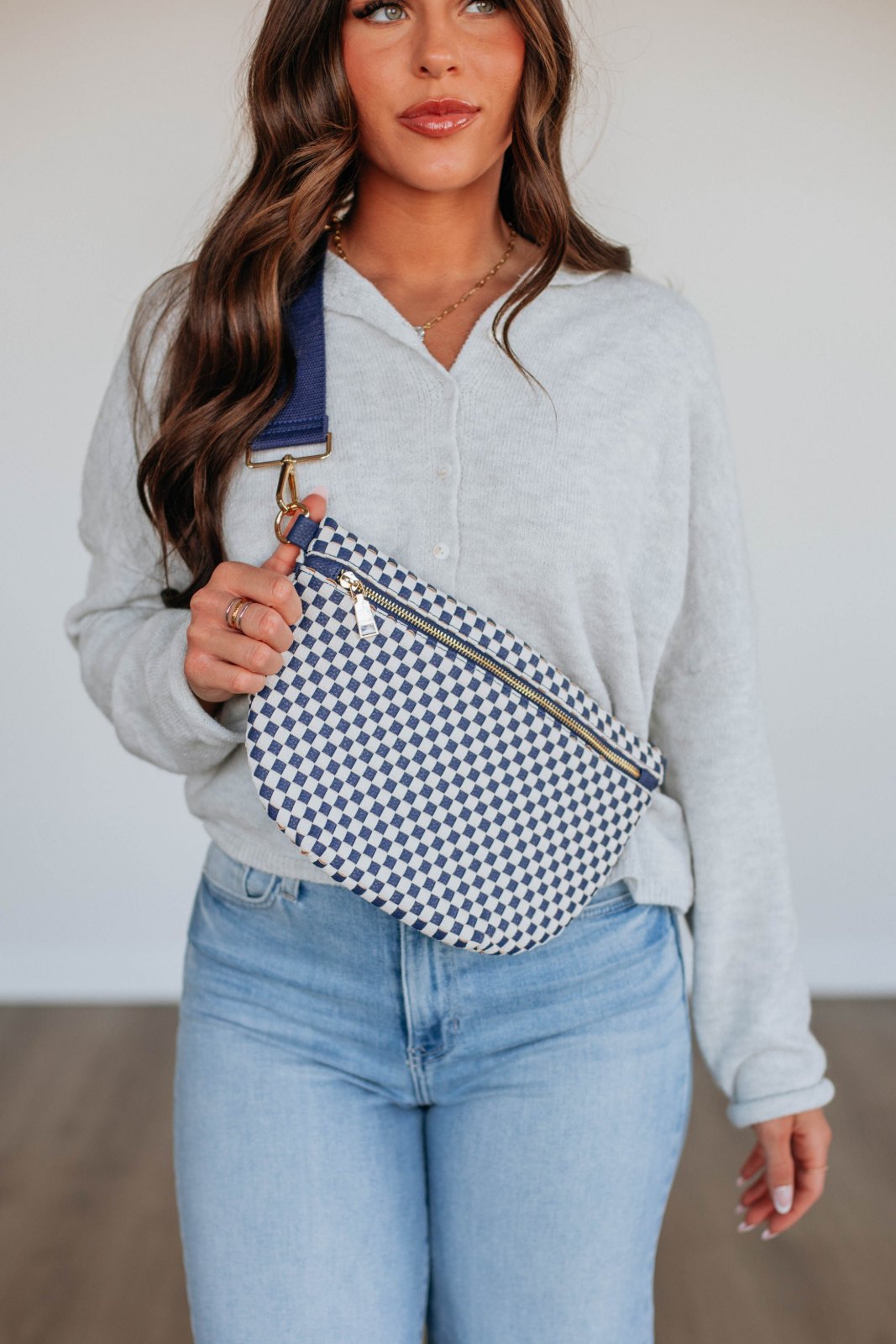 Un sac banane en tissu motif pied-de-poule, généralement porté en bandoulière pour un style décontracté et pratique. 