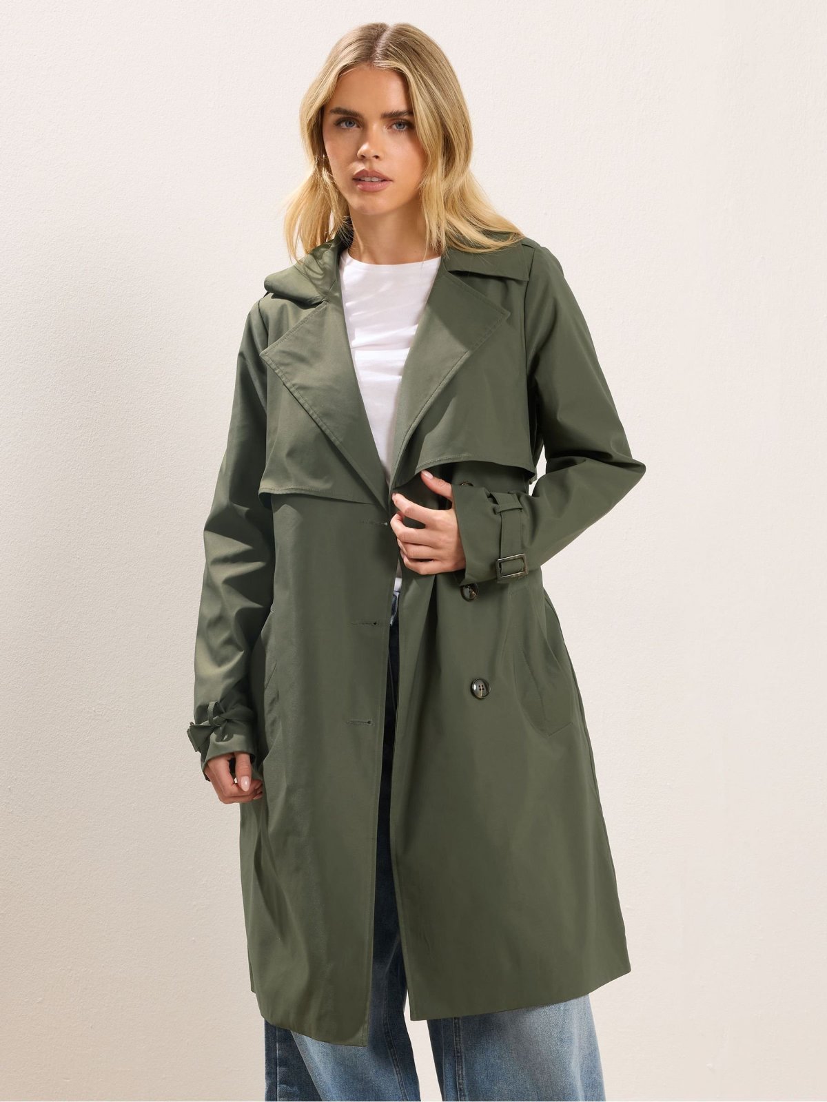 Un trench-coat pour femme de couleur vert olive, doté d'une doublure à rayures bleues et blanches.
