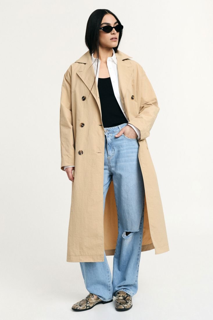 Trench-coat beige de la marque MANGO est un vêtement classique et élégant, caractérisé par sa double boutonnage et sa coupe structurée. 
