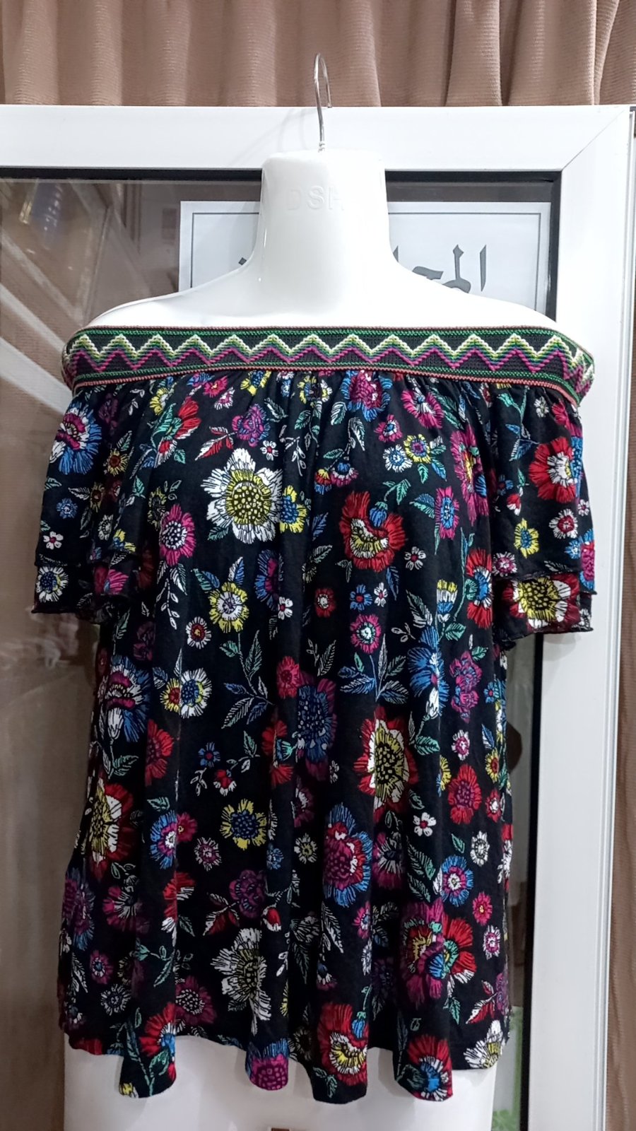 Haut yessica à épaules dénudées présente un motif floral vibrant sur fond noir et des manches à volants