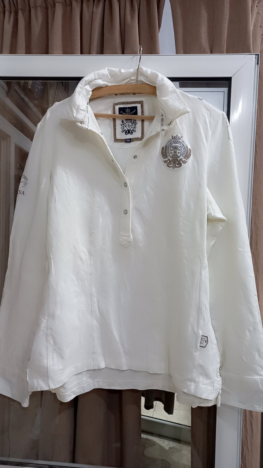  polo de couleur blanche avec des écussons décoratifs.