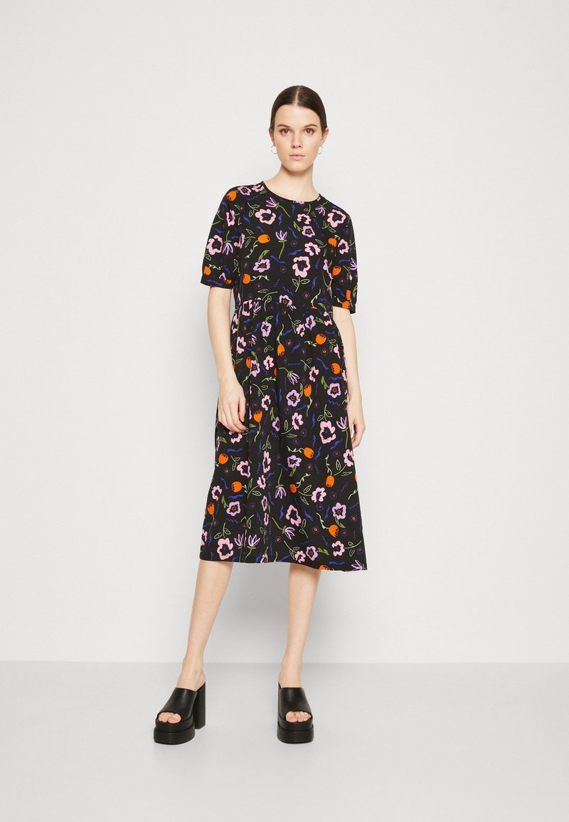 Une robe Monki à motif floral multicolore sur fond noir avec des manches courtes et une coupe décontractée