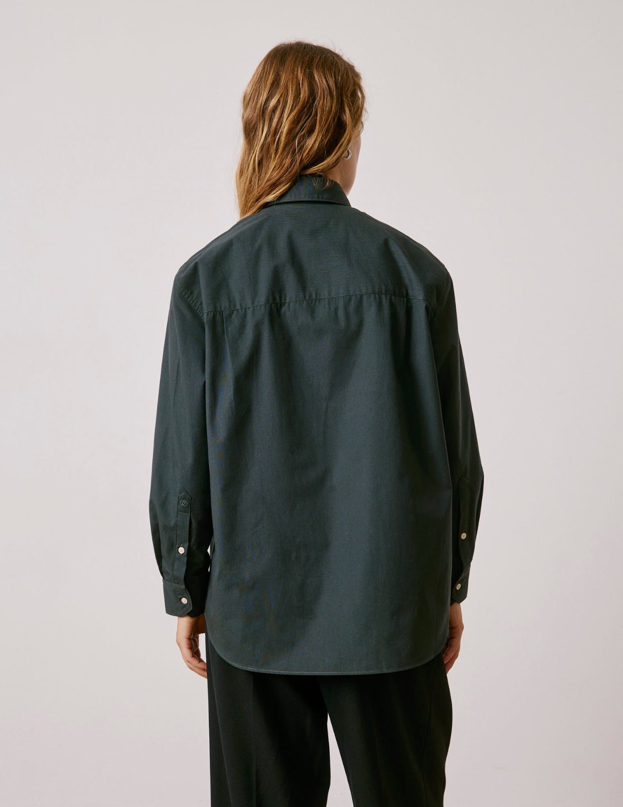 Une chemise ample à manches longues de couleur vert militaire foncé de boutons contrastants clairs sur le devant.    