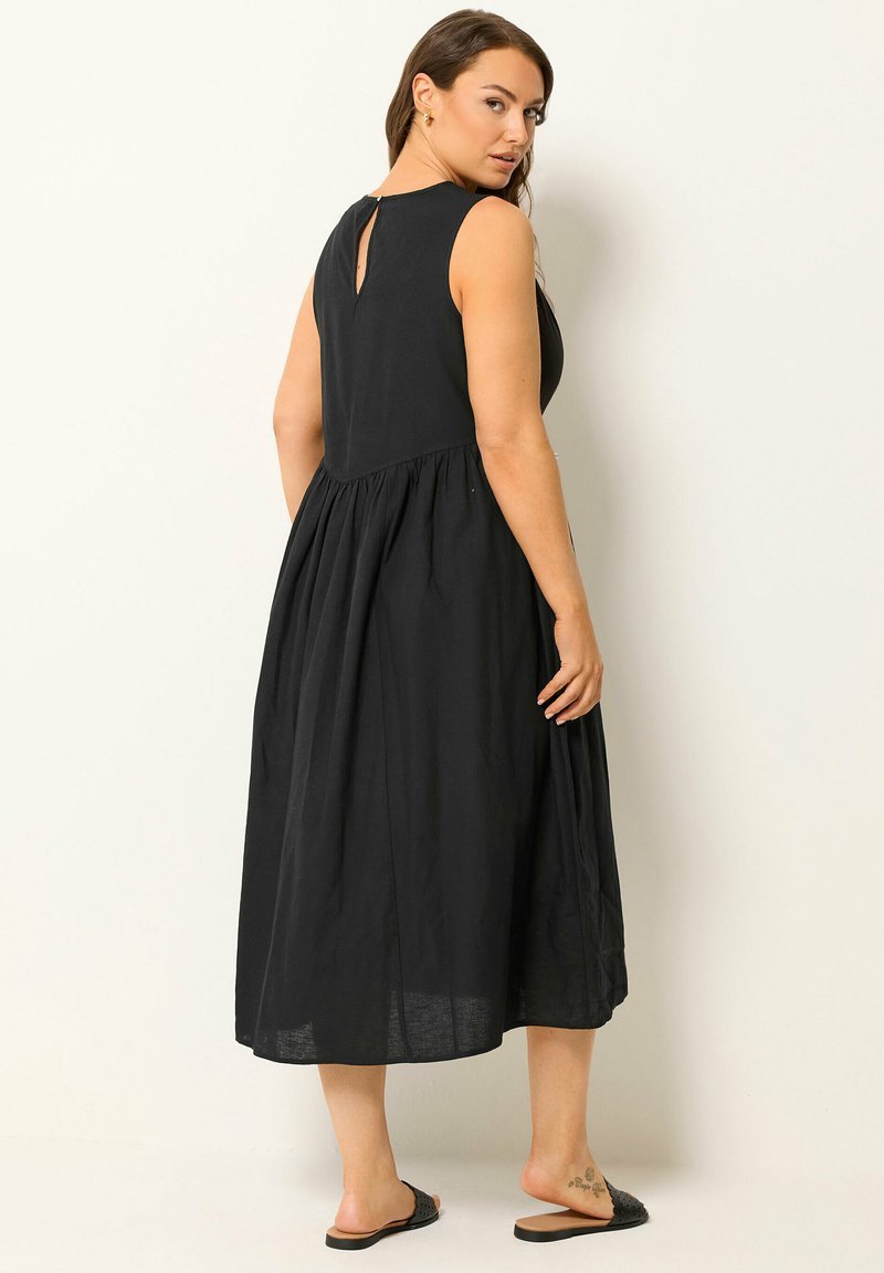  robe sans manches noire présente un haut plissé délicat, des détails en dentelle et une jupe évasée à plusieurs niveaux. 
