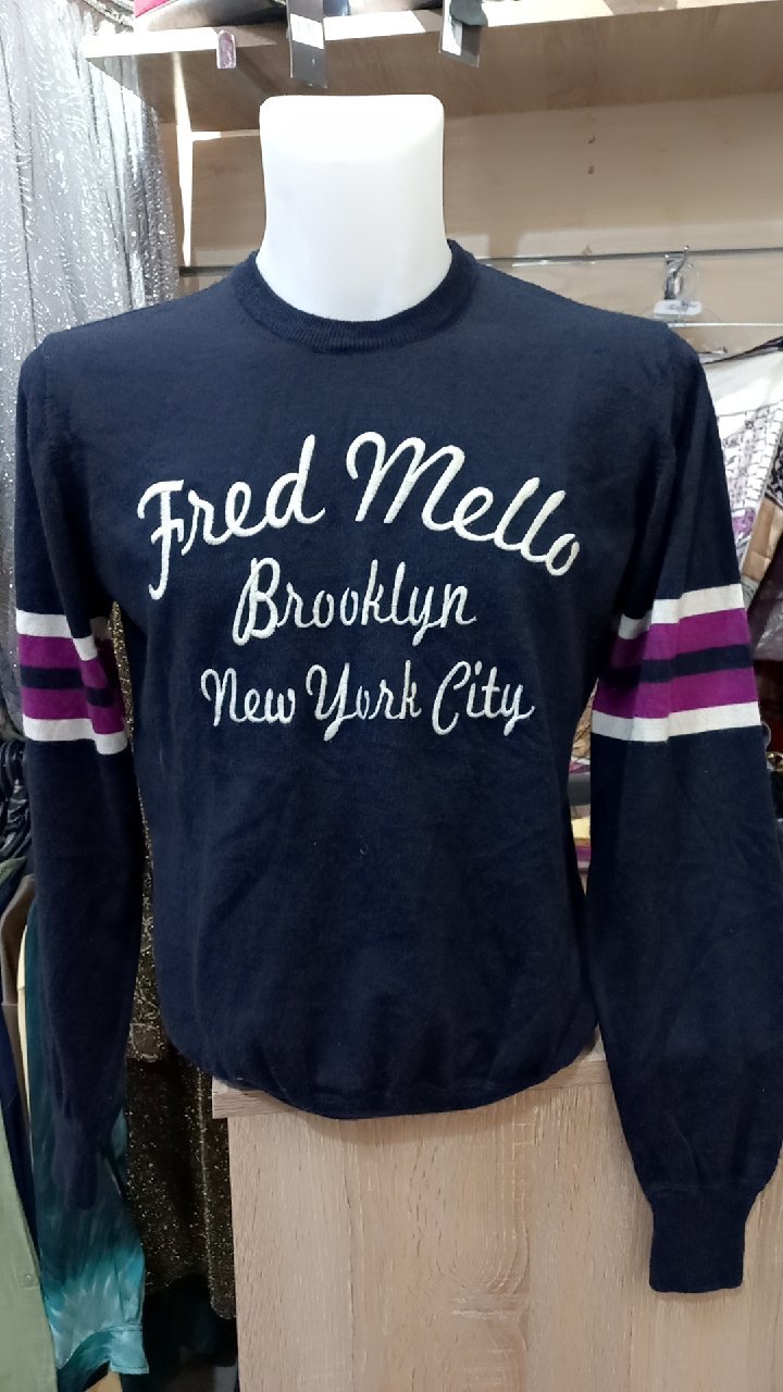  pull Fred Mello bleu marine à manches longues avec des rayures violettes et blanches sur les manches.