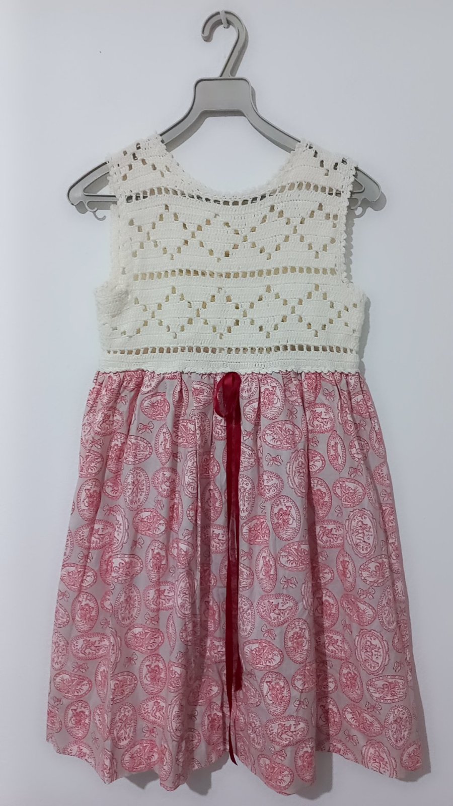 Robe enfant présente un haut en crochet blanc et une jupe en tissu rose à motifs.