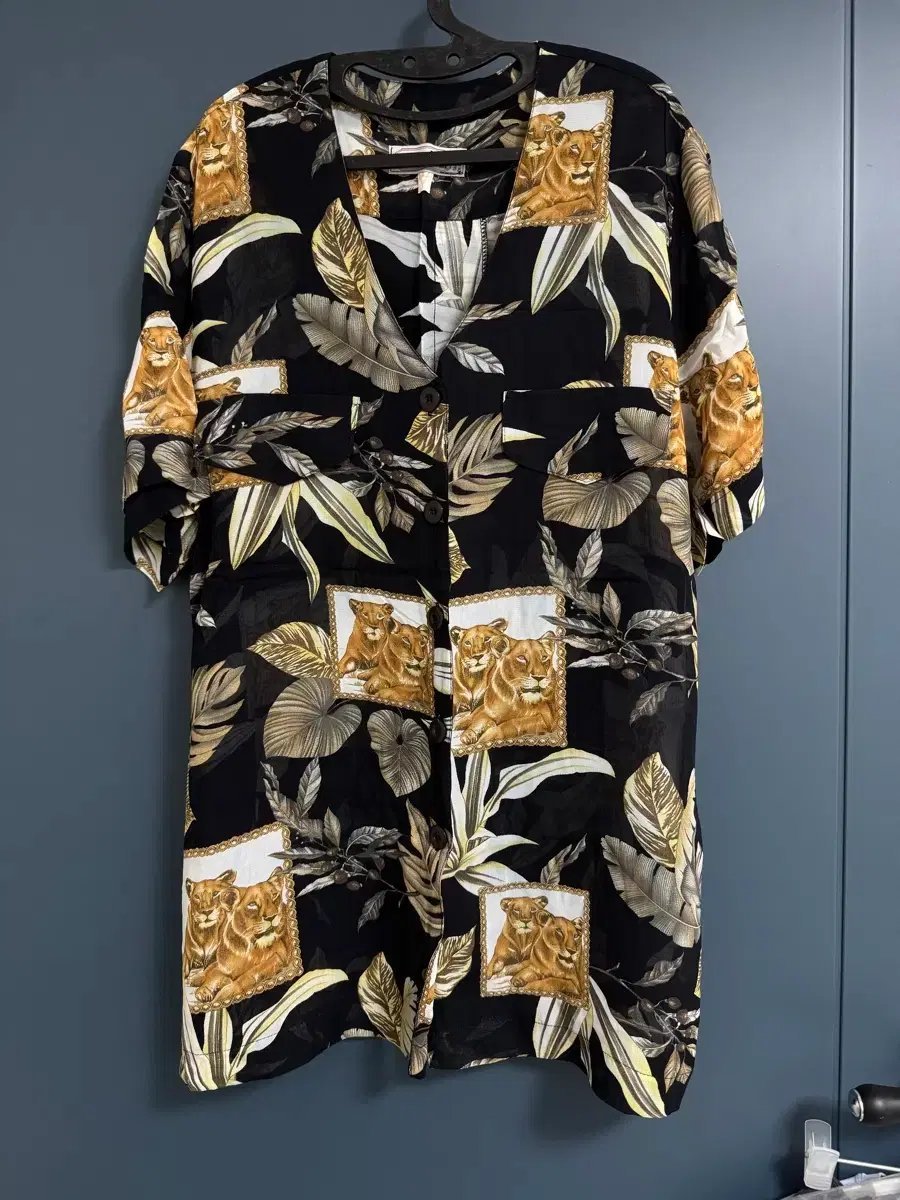 Chemise hawaïenne vintage présente un fond noir élégant orné d'un motif tropical de feuilles beiges et vertes, complété par des cadres illustrant des lions