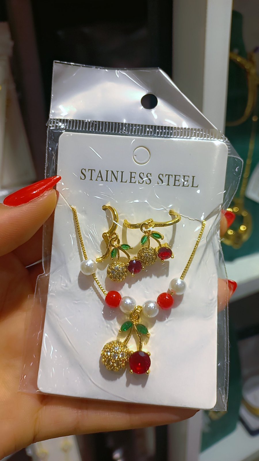 Ensemble de bijoux en acier inoxydable arbore des pendentifs en forme de cerises ornés de zircons rouges et verts.