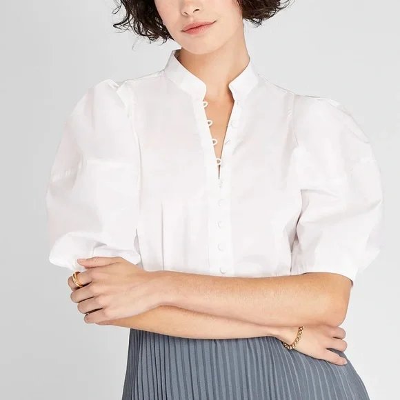 Un chemisier blanc pour femme, doté de manches bouffantes et d'une fermeture à boutons sur le devant.