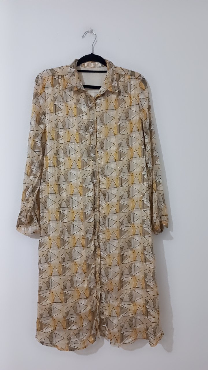Une robe-chemise longue et fluide à manches longues, ornée d'un motif géométrique abstrait aux tons beiges et jaunes.    