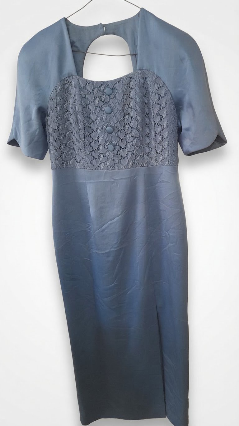 Une élégante robe mi-longue de couleur bleu poudré, caractérisée par un haut en dentelle texturée rehaussé de boutons décoratifs assortis sur le devant.    
