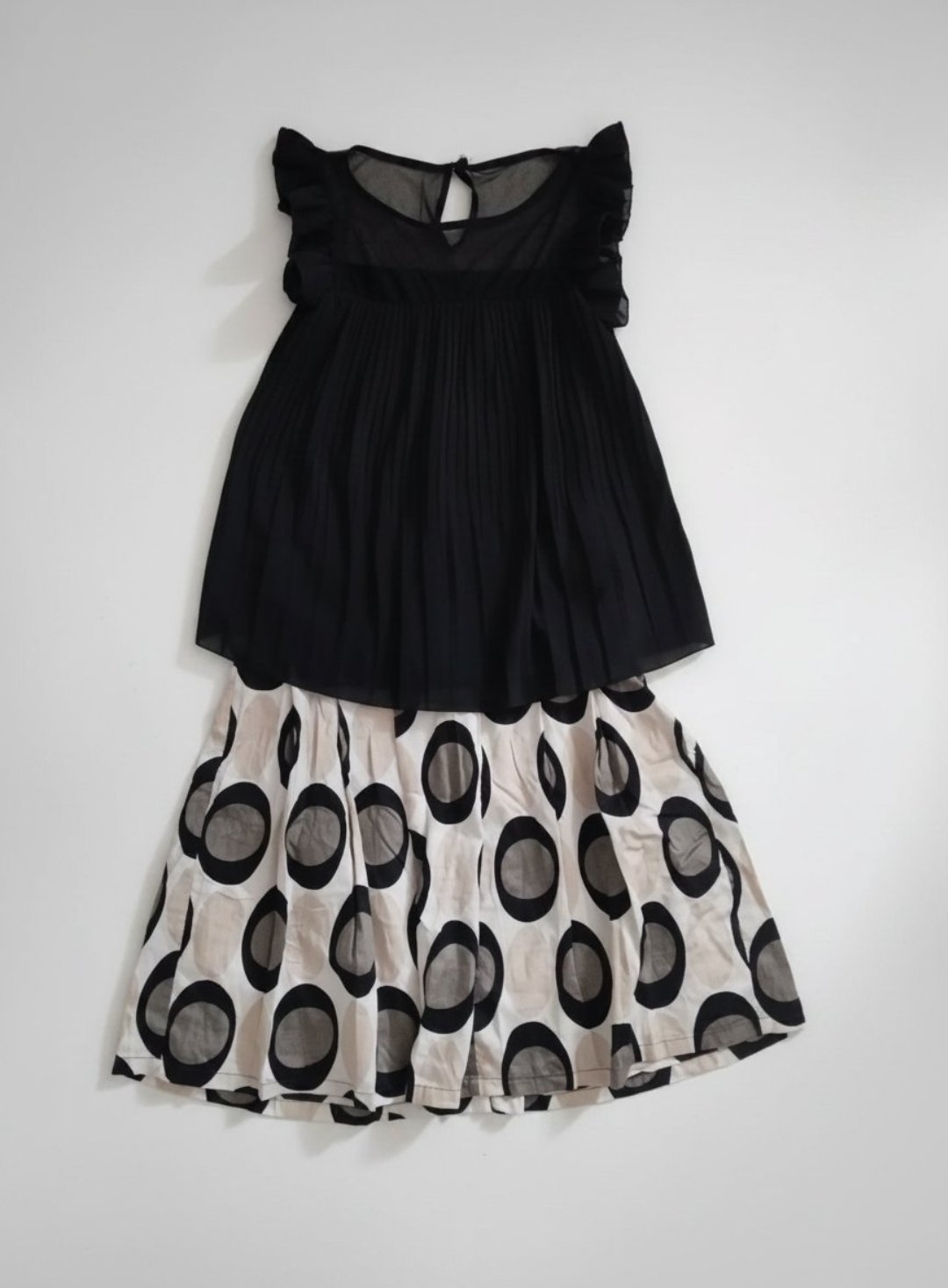 Cet ensemble se compose d'un haut noir plissé sans manches avec des volants aux épaules et d'une jupe blanche à motifs circulaires noirs et gris.