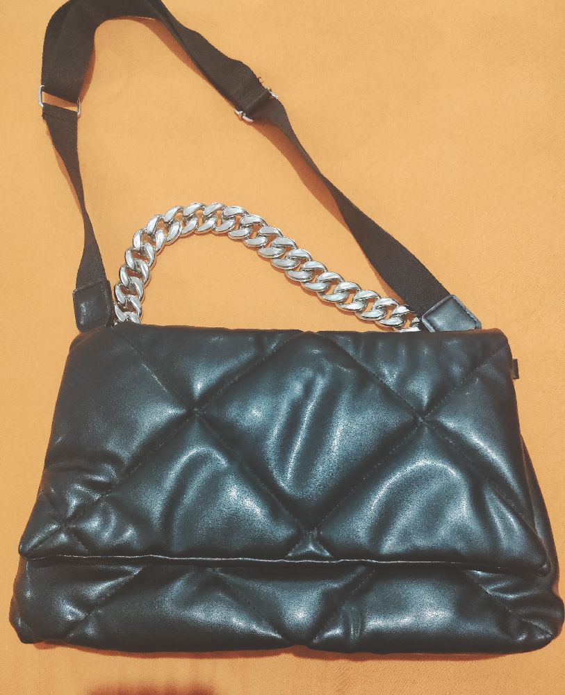 Un sac noir avec une chaîne argentée et une bandoulière.