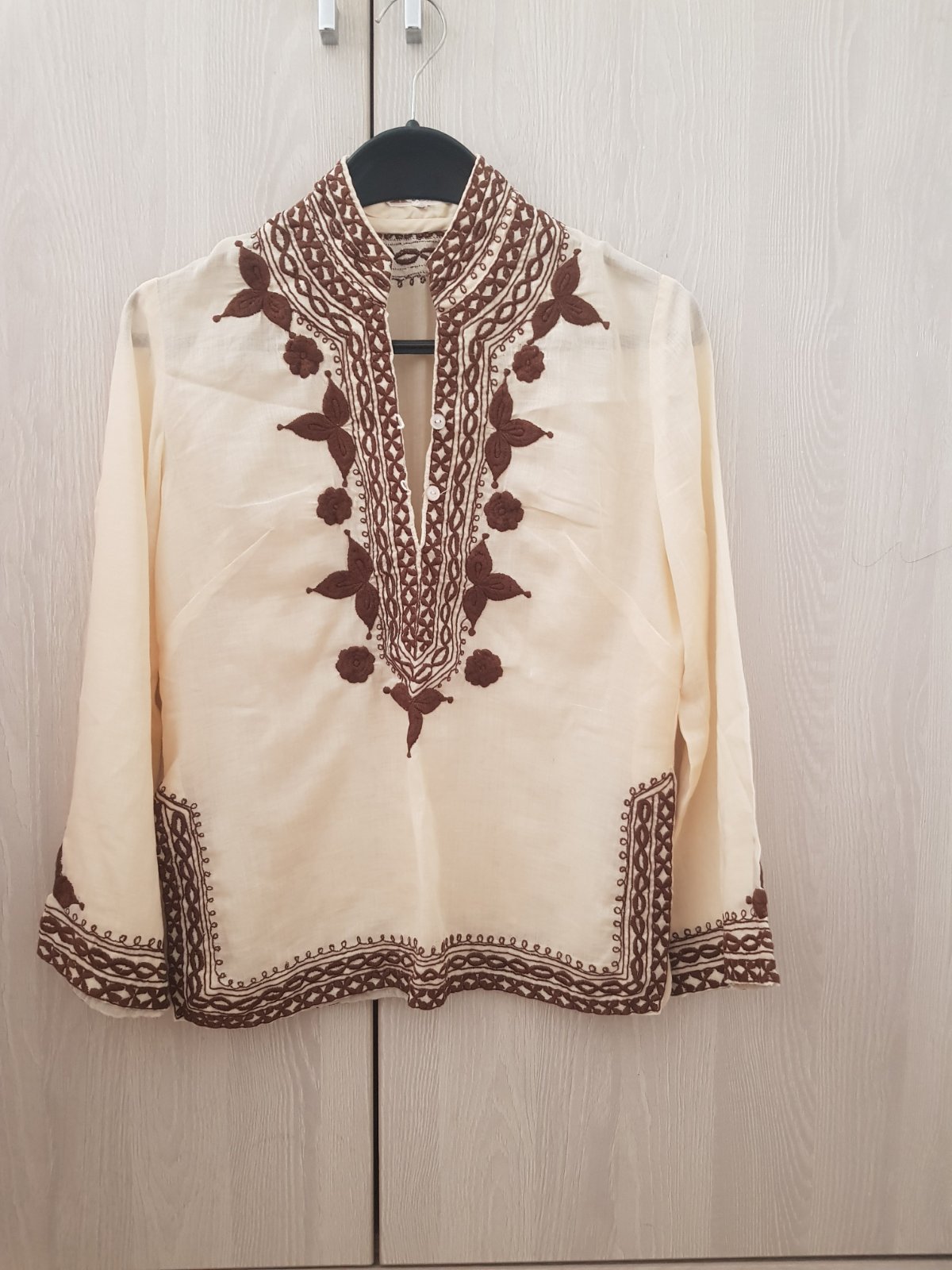 Tunique boho écru à manches longues avec une broderie marron le long du col en V, de la patte de boutonnage et des poignets. Tissu coton 