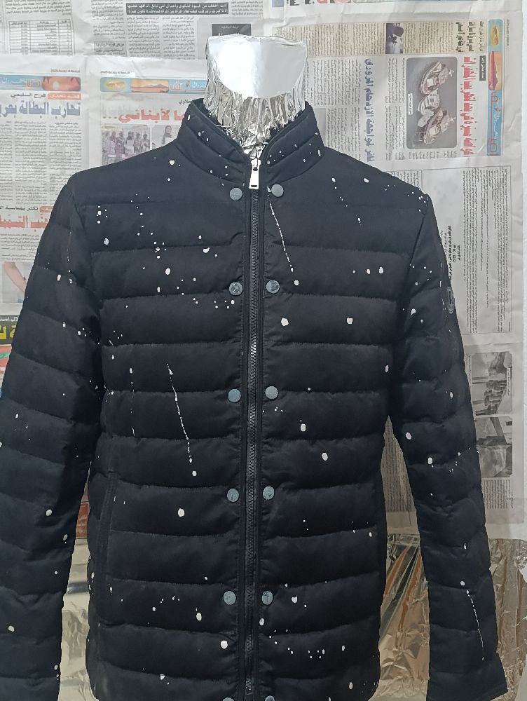 Blouson doudoune noir arbore un motif d'éclaboussures de peinture blanches, un style populaire dans la mode urbaine et contemporaine. 