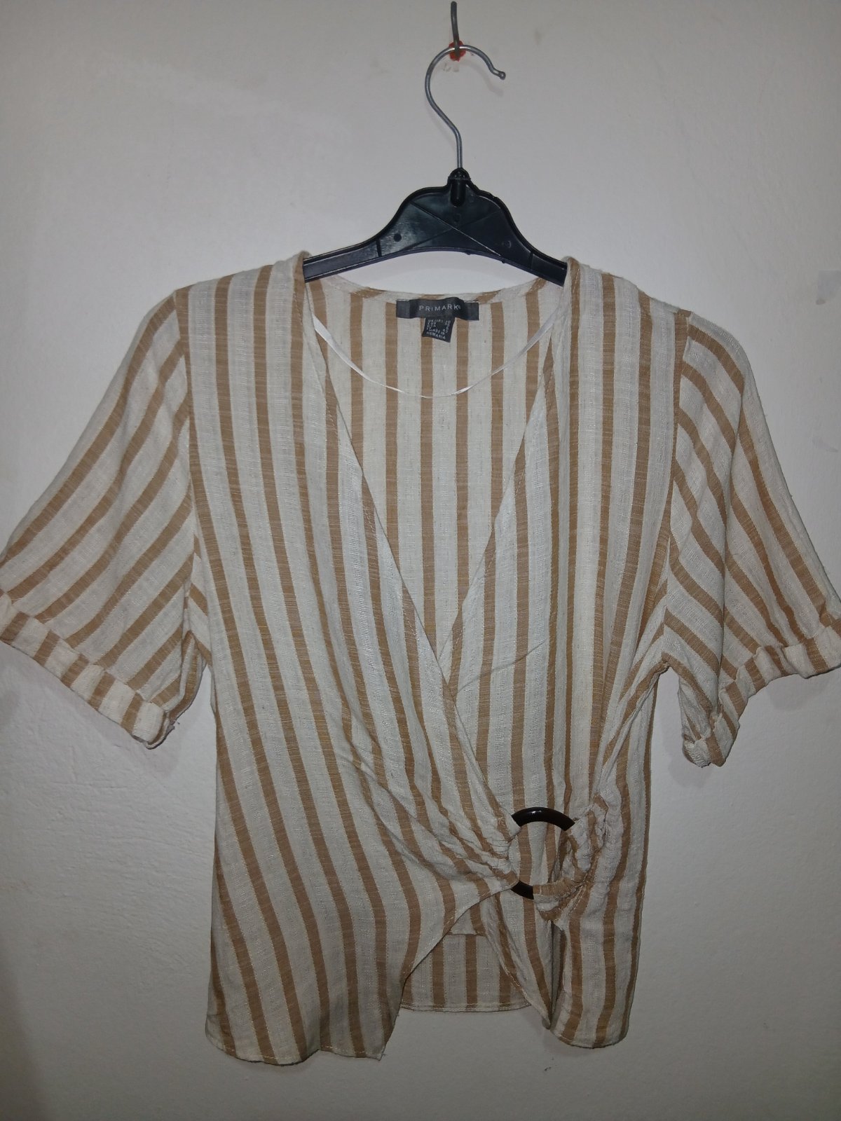              Cette blouse Primark à rayures beiges et blanches est fabriquée avec un mélange de lin et comporte un nœud décoratif sur le côté.