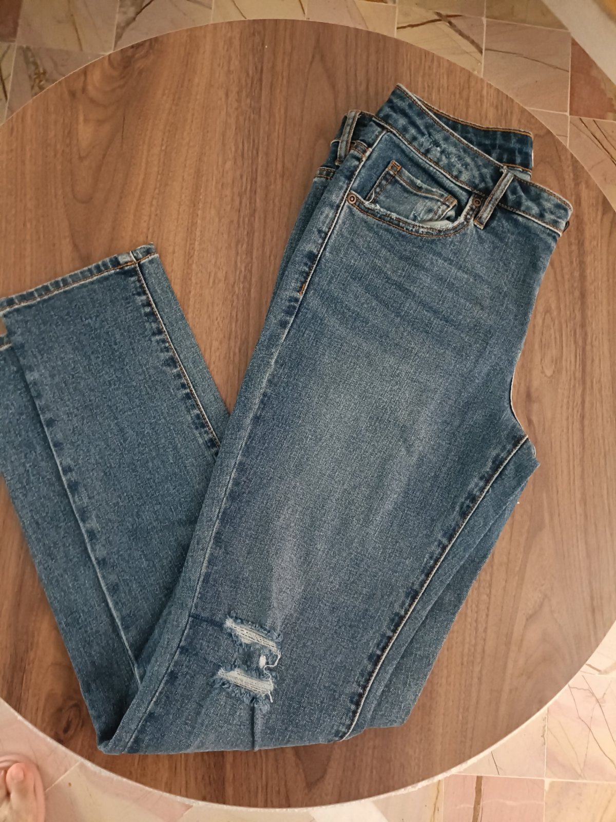Jean skinny bleu moyen à taille mi-haute présente un léger effet délavé et une déchirure décorative au niveau du genou.