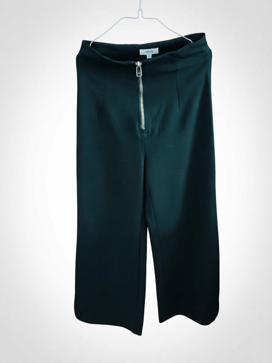 Pantalon noir taille haute à jambes larges avec une fermeture éclair dorée apparente sur le devant.
