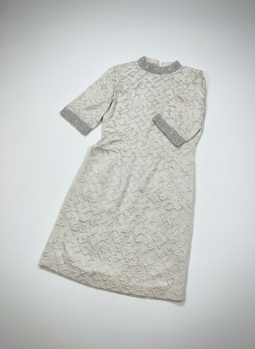 Robe de soirée beige et argentée arbore une texture brodée distincte et des détails scintillants sur le col et les manches