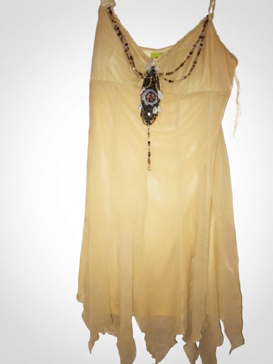 Robe légère et fluide de couleur jaune pastel, idéale pour la saison estivale. ✨ Style bohème avec un joli collier décoratif en perles et coquillages intégré. 👗 Coupe féminine avec finition asymétrique au bas de la robe.