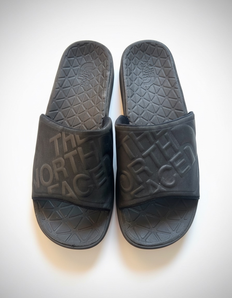 Ces claquettes noires sont des The North Face, reconnaissables à leur grand logo en relief sur la bride