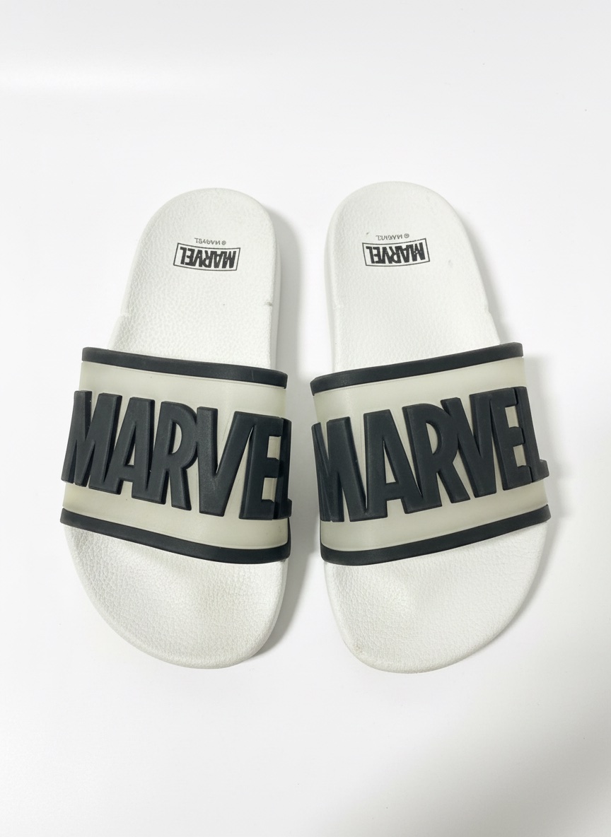 Ces claquettes sont des sandales de style pool slider avec une large bride blanche arborant le logo Marvel en noir.