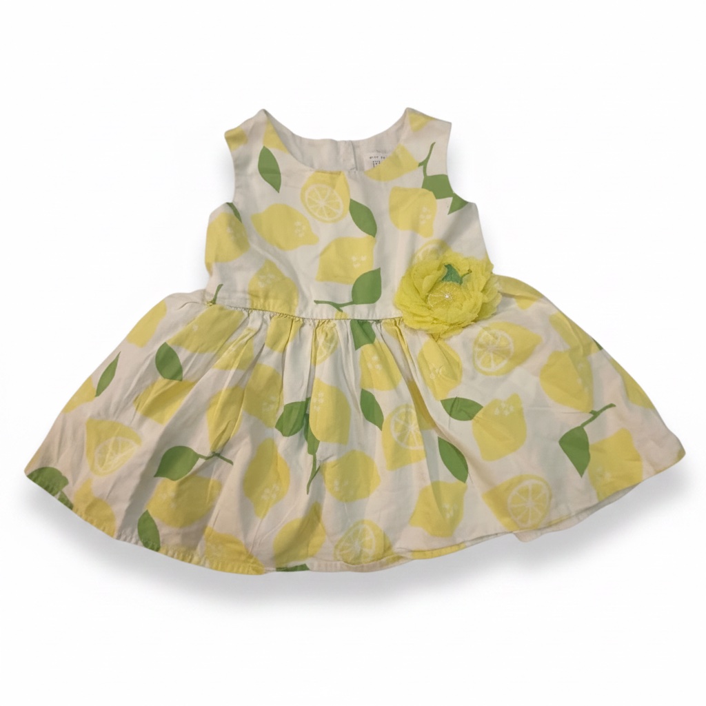 Cette robe sans manches pour bébé fille de The Children's Place présente un motif intégral de citrons jaunes et de feuilles vertes sur fond blanc, agrémentée d'une fleur jaune en tissu sur le côté gauche.