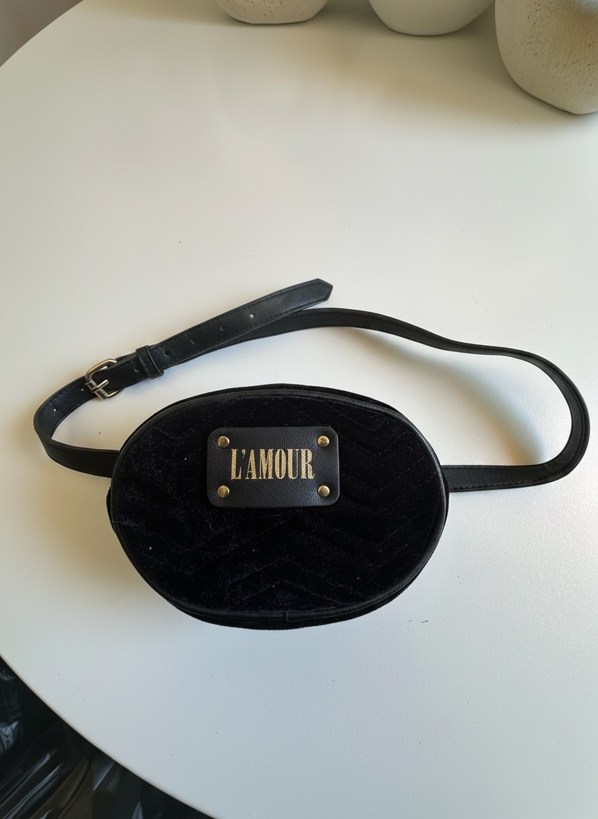 Ce sac banane noir en velours arbore une plaque métallique avec l'inscription "L'AMOUR"