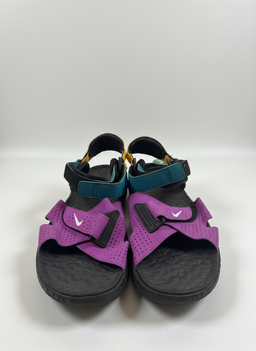 Ces sandales sont des Nike ACG Air Deschutz dans le coloris "Vivid Purple" avec des détails en bleu et jaune.