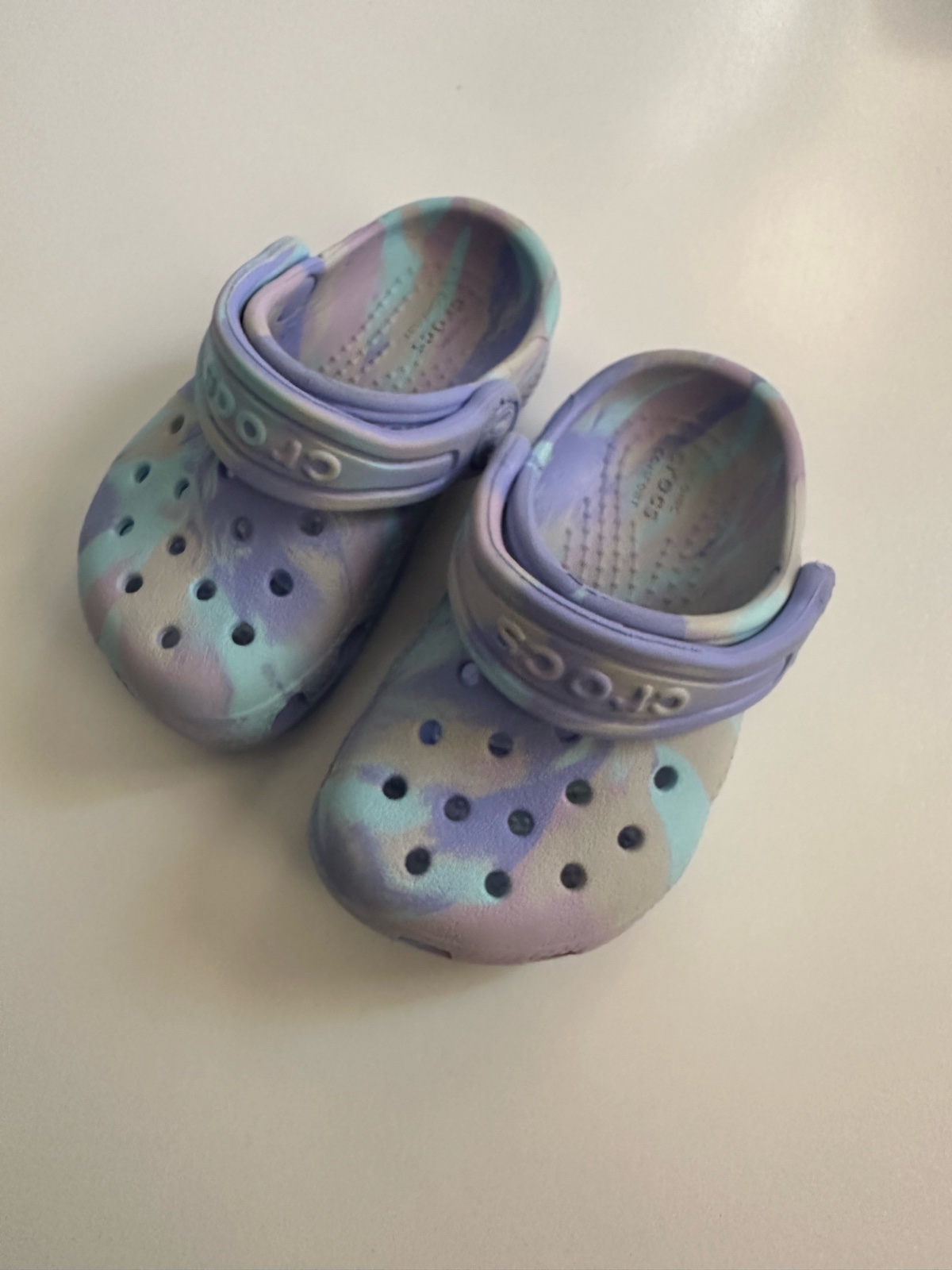 Ces sabots pour enfants sont des Crocs Classic Marbled Clog affichant un motif tie-dye bleu et violet unique
