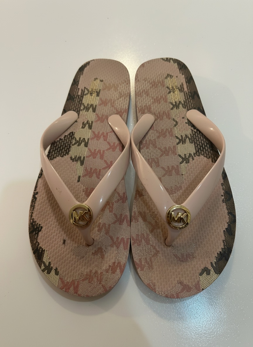  Ces tongs Michael Kors présentent une semelle à motif logo emblématique et une bride rose poudré ornée d'un médaillon doré